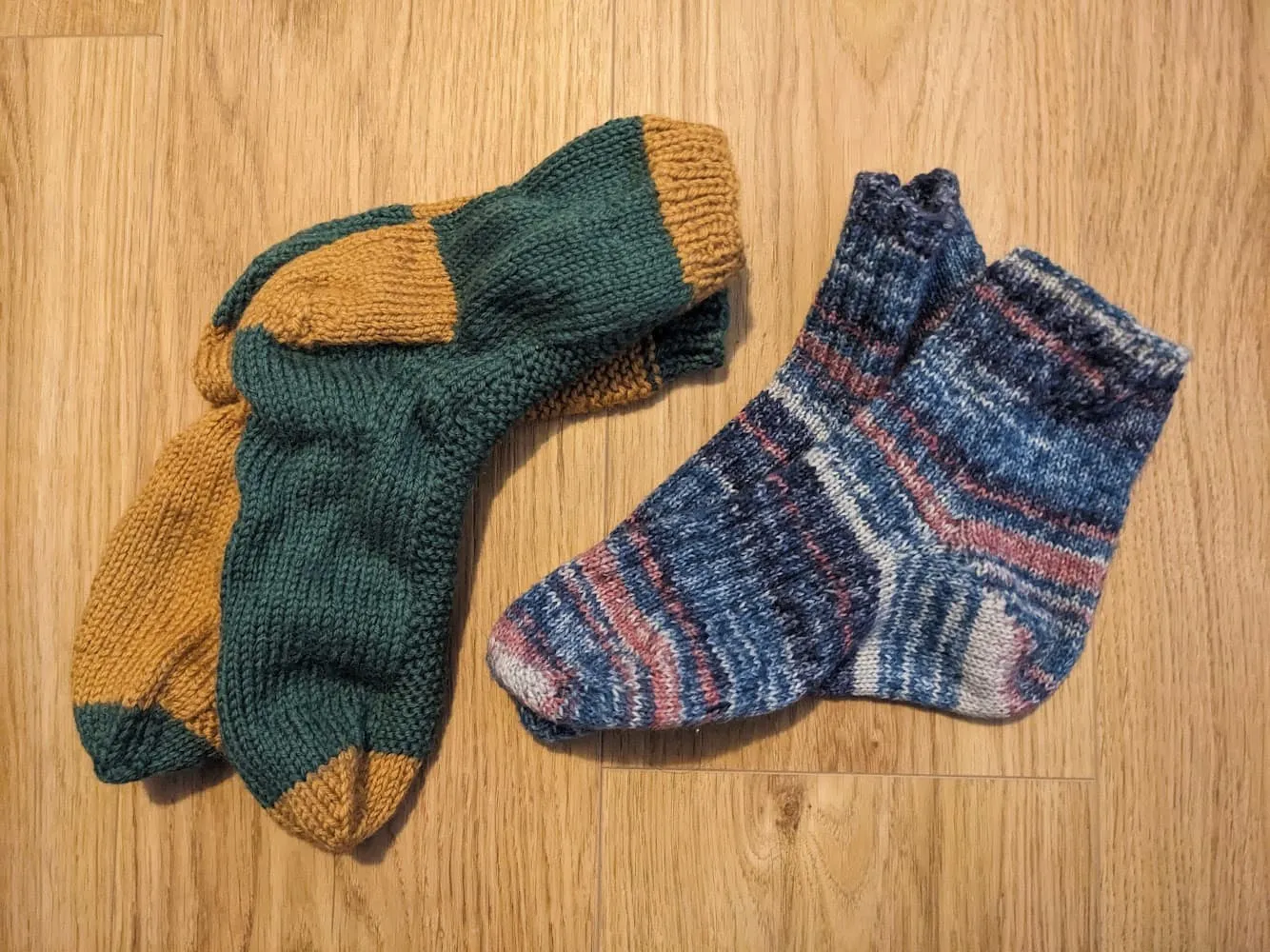 two pairs of knitted socks. one pair is yellow and green, and the other uses self-striping yarn with blues and whites and reds