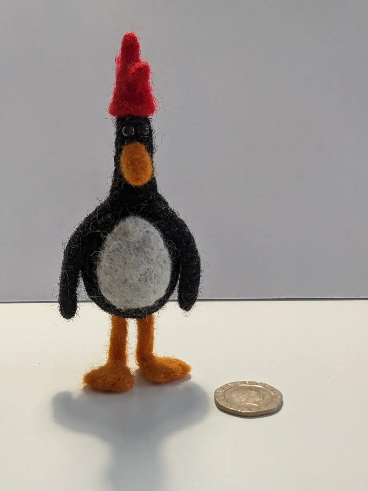a needle felted penguin with a red gloved-shaped hat. it's the penguin/chicken from wallace and gromit